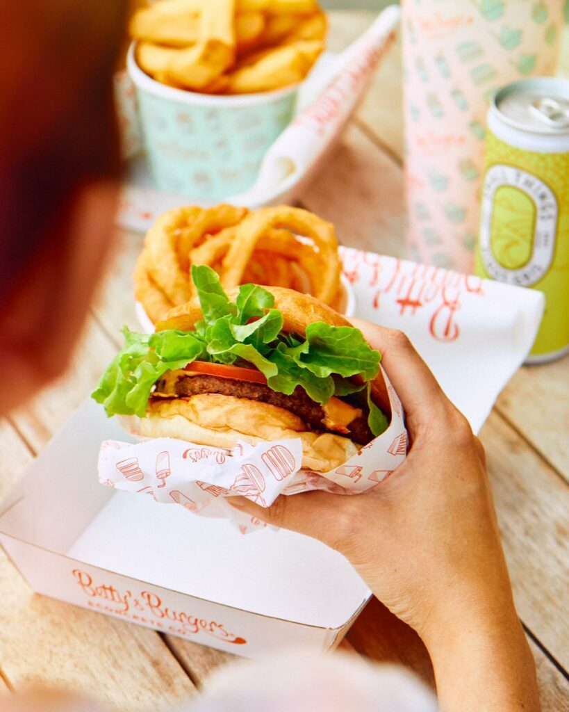 A plant-based burger is being held up from its takeaway container from Betty's Burgers.