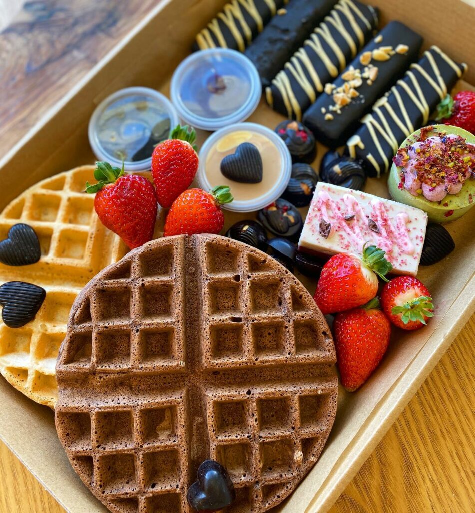 An overhead shot of a takeaway tray full of waffles, chocolate, berries, chocolate bars, and various other desserts.