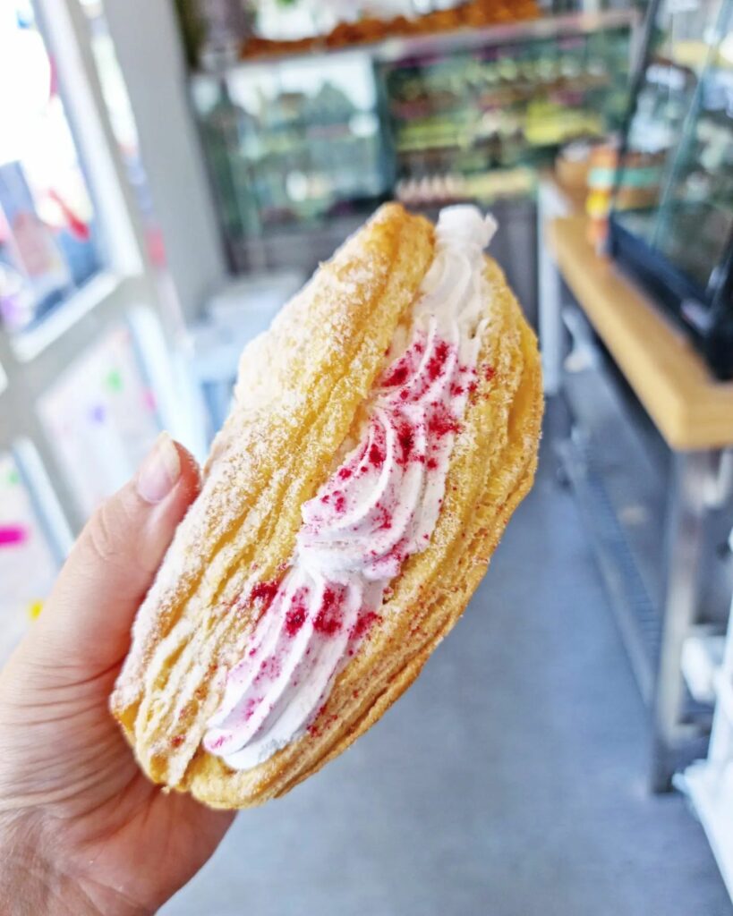 A hand holds up a apple turnover, with the cream side turned to camera. It's decorated with a pink sugar.