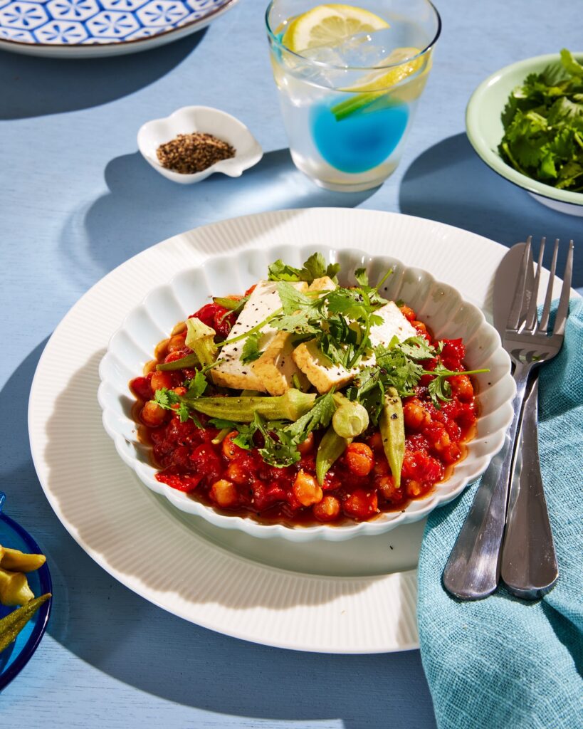 A table set beautifully with a blue theme, with a bowl of hearty looking tofu and okra shakshuka.