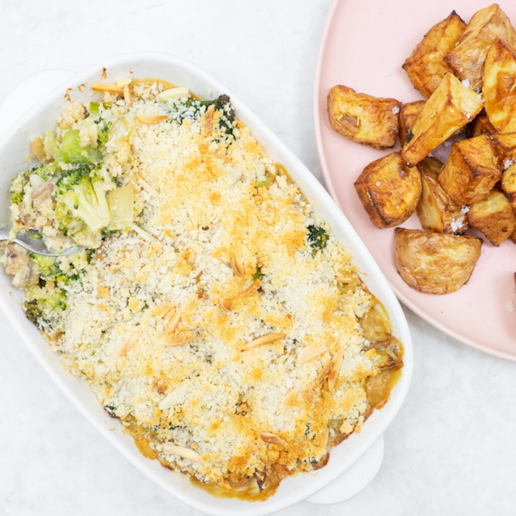 An overhead image of a bakes broccoli casserole next to a plate with a side of roast potatoes.