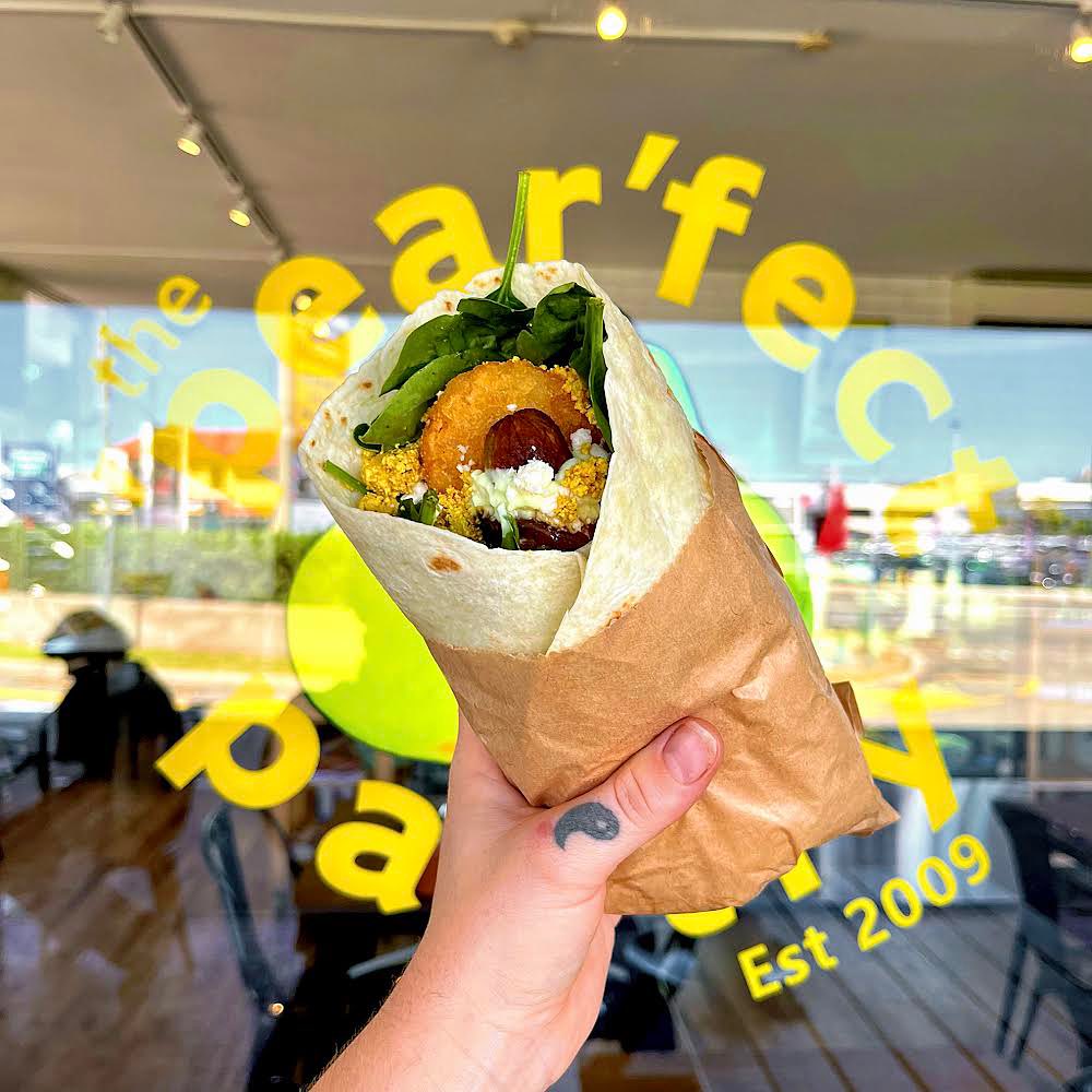 Image of a hand holding up a delicious looking breakfast wrap in front of The 'Pear'fect Pantry window sticker. 