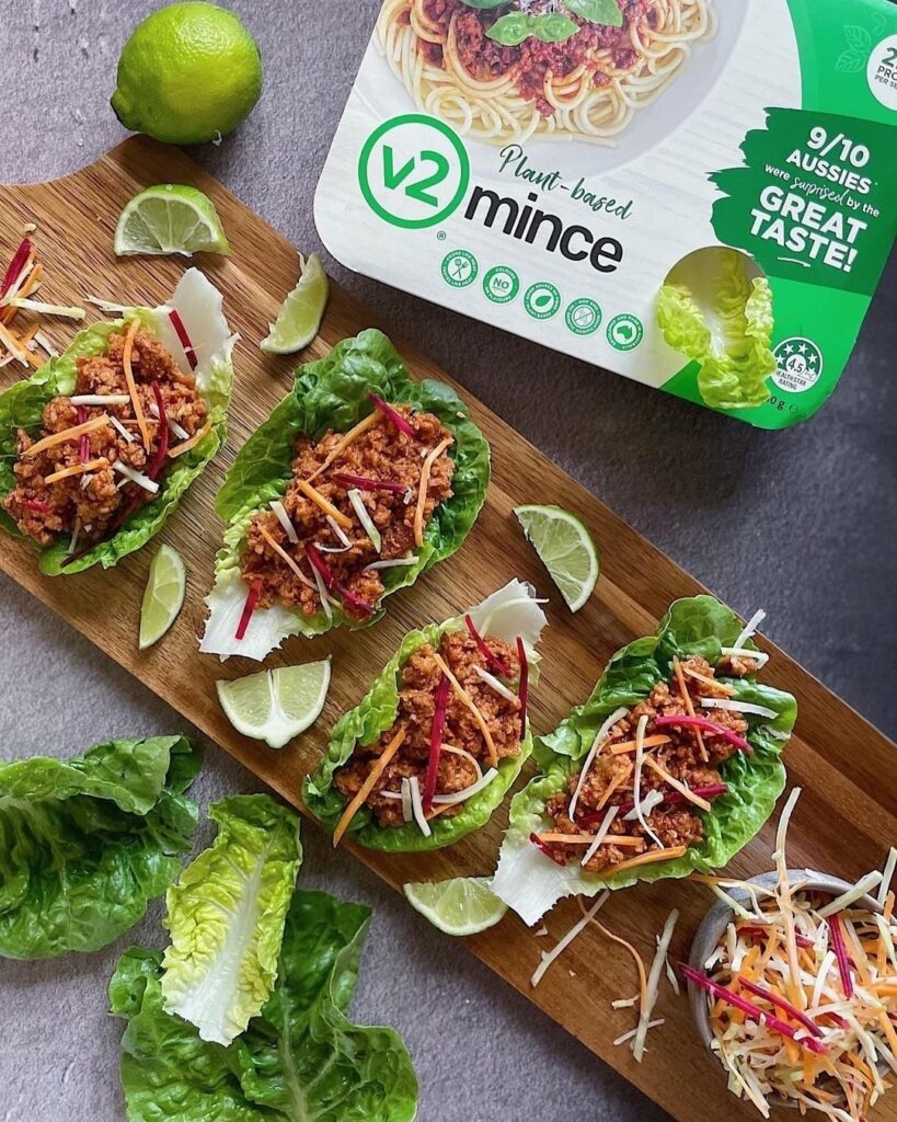 A wooden serving board is full of plant-based mince in cups of lettuce.