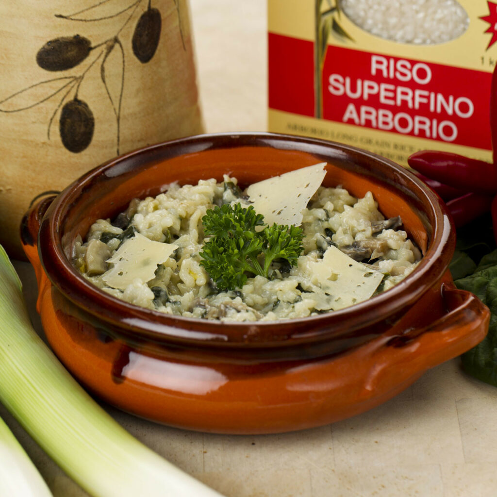 A bowl of spinach and mushroom risotto sits on a bench surrounded by its ingredients.