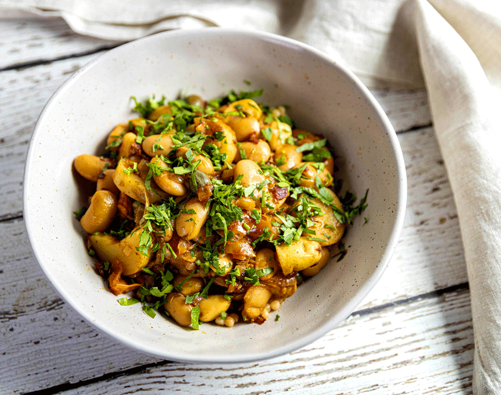 A close-up image of a potato and bean stew with almonds, garnished with parsley. 