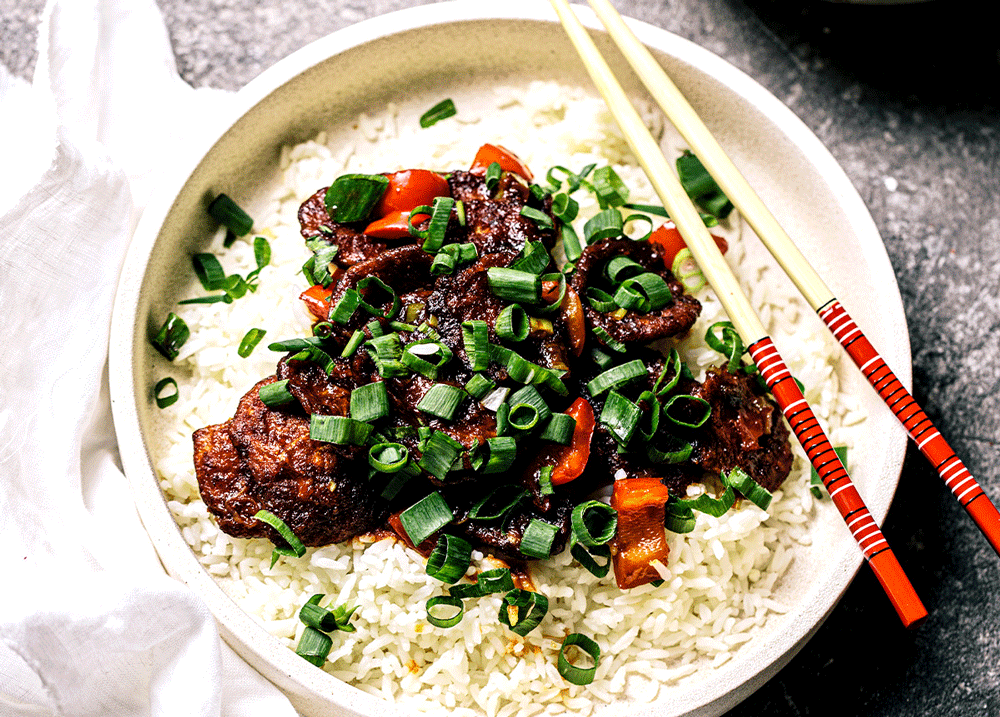 A stirfry on a bed of white rice with plant-based beef strips, garnished with spring onion. 