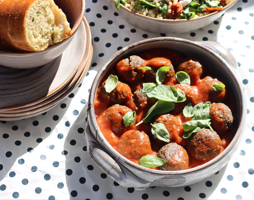 A small bowl of mushroom 'meatballs' in a rich red sauce, topped with basil leaves. A crusty breadstick is just in shot.