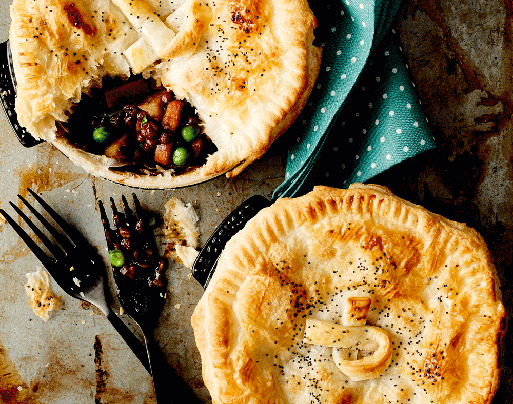 Two individual opt pies sit side by side. One has been broken open with a fork to show a very hearty looking centre of mushroom, gravy and veg.