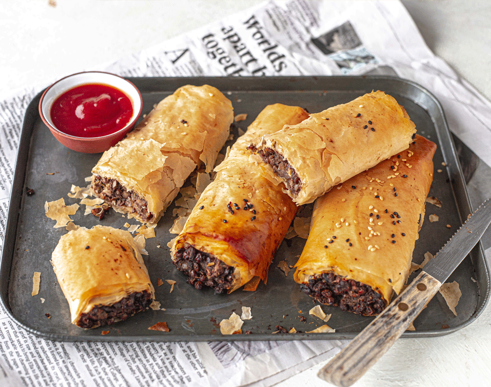 A tray of four sausage rolls, a few cut open to show a meaty looking centre. The pastry is perfectly flaky.