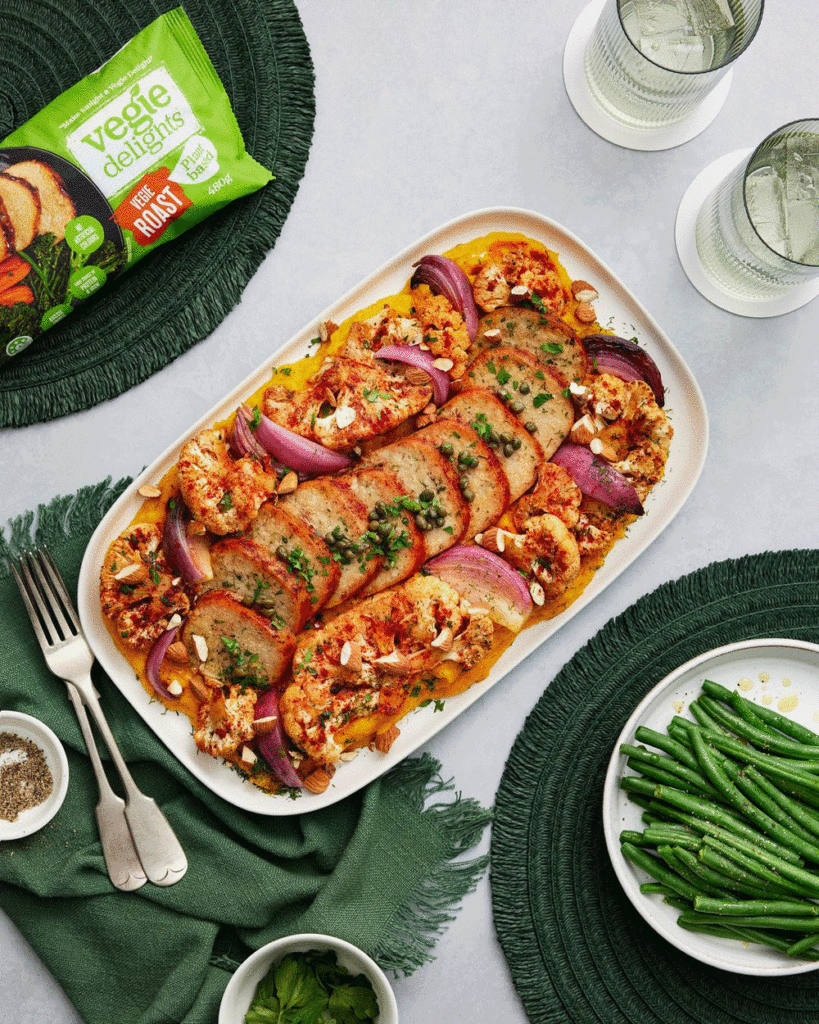 An overhead shot of a serving platter with servings of Vegie Delights plant-based roast, surrounded by roast veg and garnished with greens.