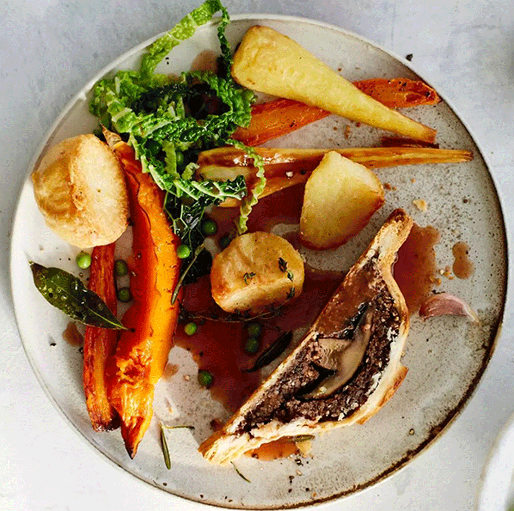 An overhead image of a plate of roast vegetable with a mushroom wellington coated in gravy.