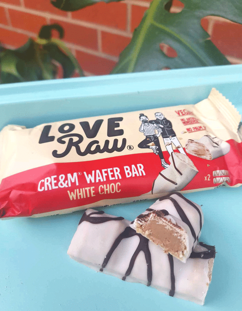 Love Raw's Cream Wafer Bar sits on a plate, showing the creamy white choc bar cut in half revealing the hazelnut and almond cream paste inside. 