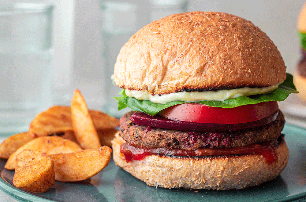 A frontal image of a simple burger on a wholemeal bun, served with a side of wedges.