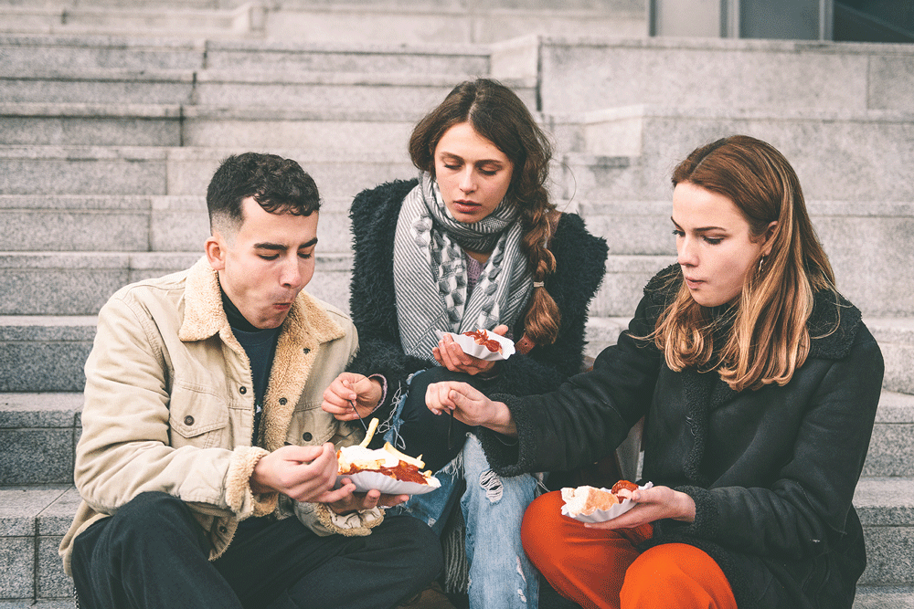 A group of three friends eat plant-based currywurst in Berlin.