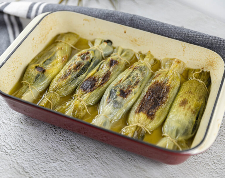 A rectangular oven tray filled with stuffed leeks in the shape of bonbons.