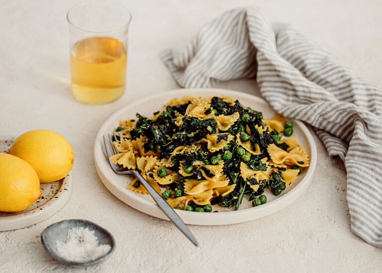 Fried Kale Pasta dish on a white plate with salt and lemons on side