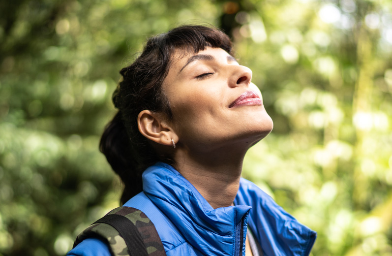 Closeup of woman's face on an outdoors hike with eyes closed breathing in looking peaceful