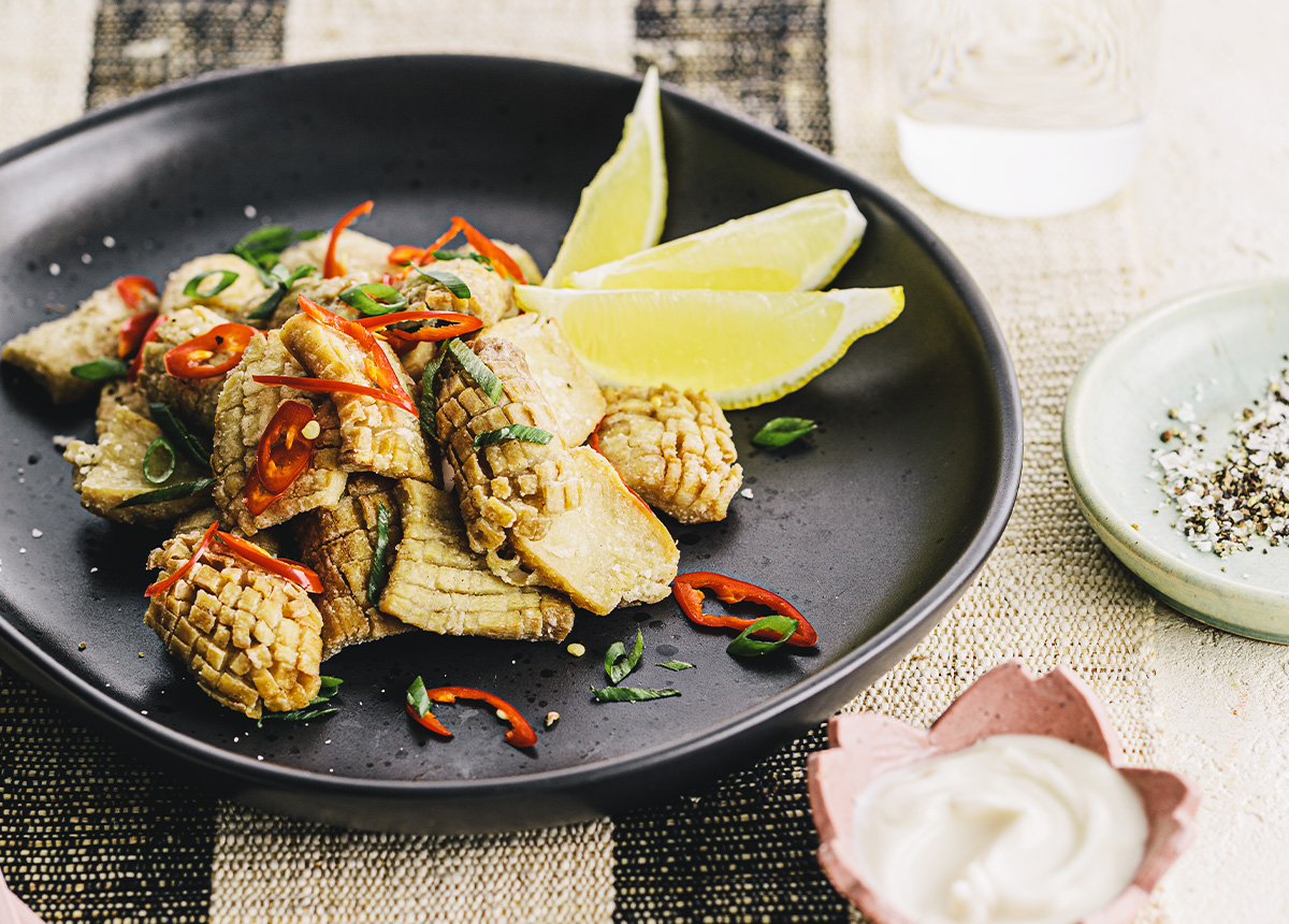 Plant-based calamari on a black plate with a wedge of lemon.