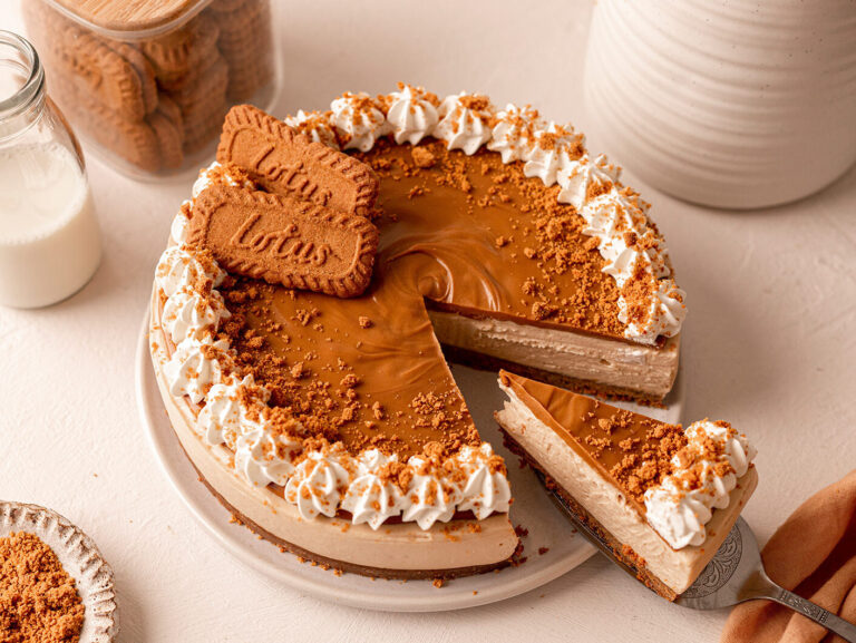 An overhead image of a decadent cheesecake on a table, beautifully decorated with a slice cut and slightly pulled out.