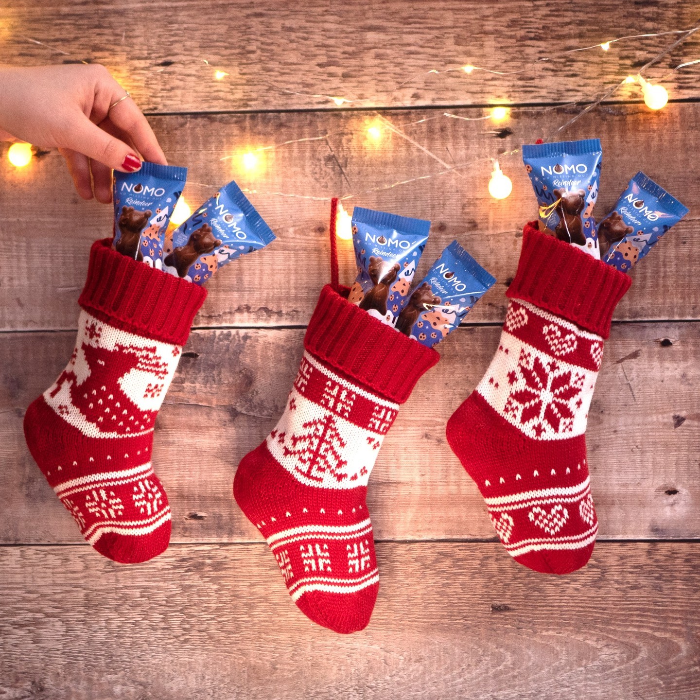 A row of three red Christmas stockings hanging, filled to the brim with Nomo chocolate reindeers.