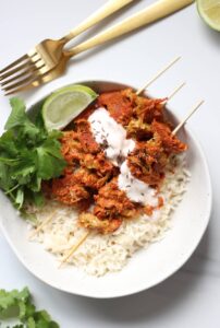 An image taken overhead of vegan tandoori chicken skewers in a bowl over a bed of rice.