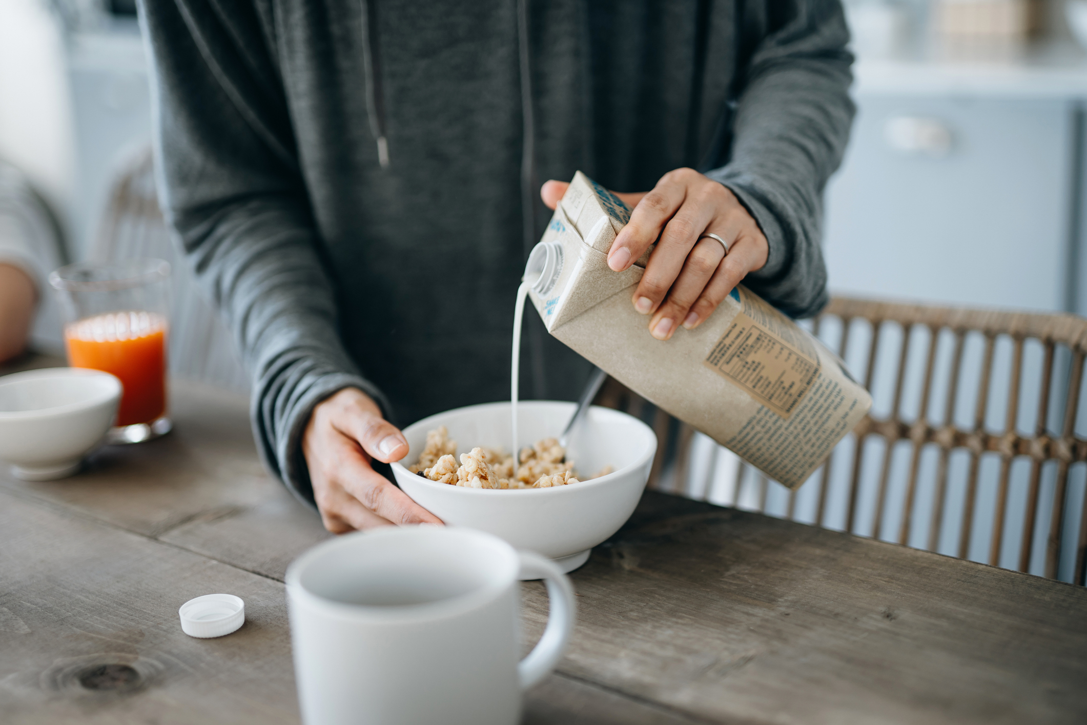 Cropped shot of a mother preparing healthy breakfast, pouring milk over cereals on the kitchen counter.