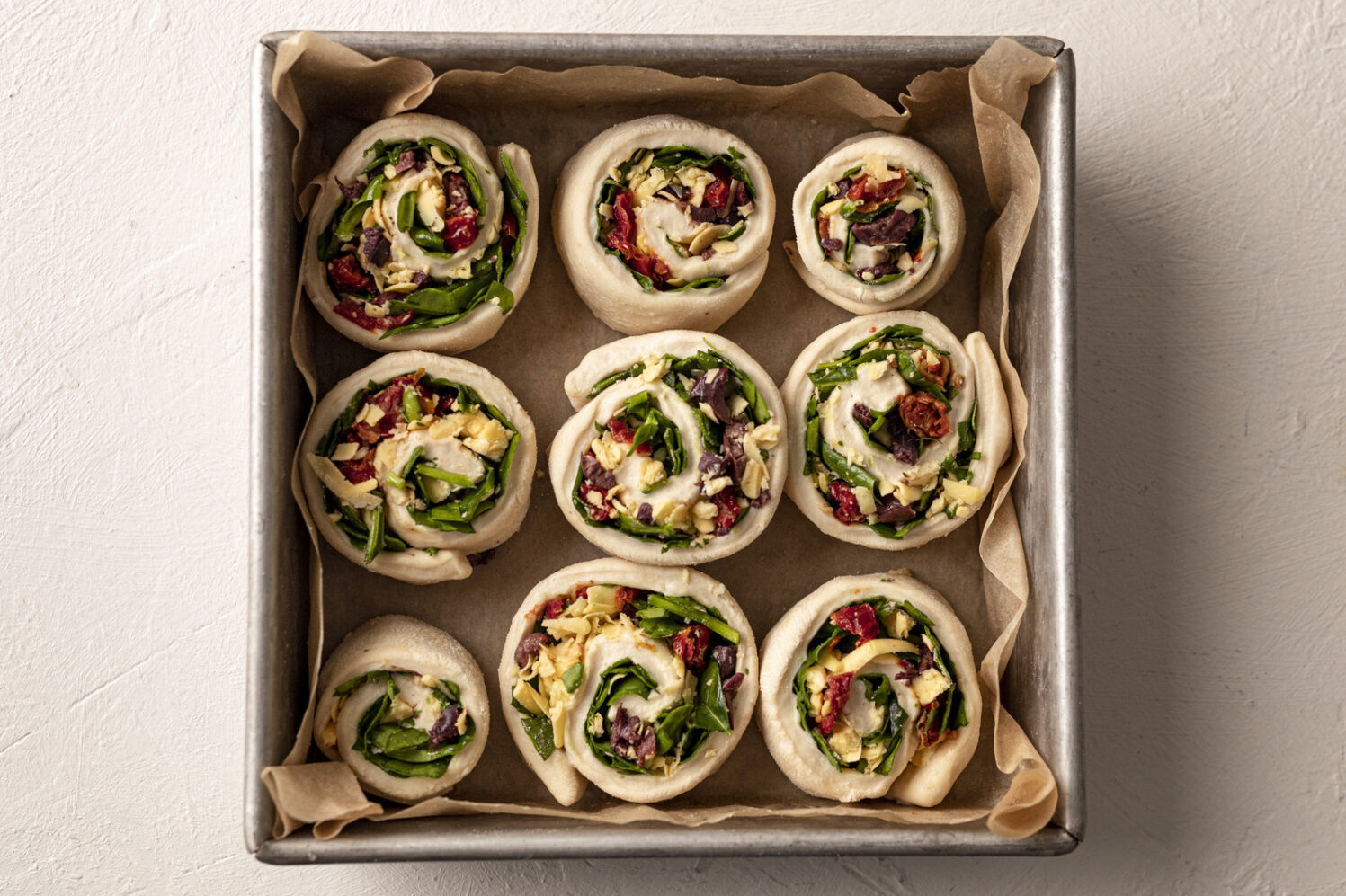 a tray of 9 pastry scrolls filled with veggies and vegan cheese