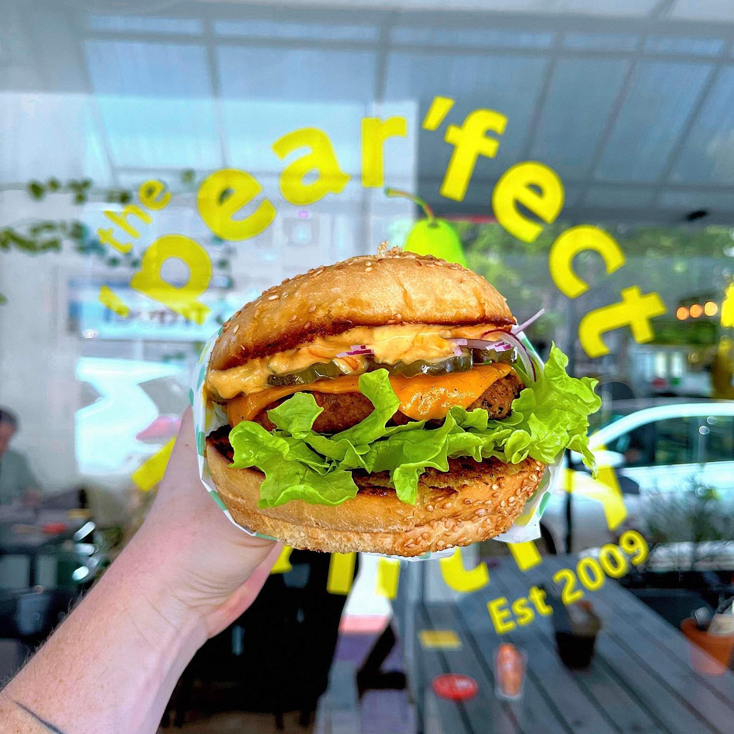 A vegan burger being held up in front of the 'Pear'fect Pantry window sign.