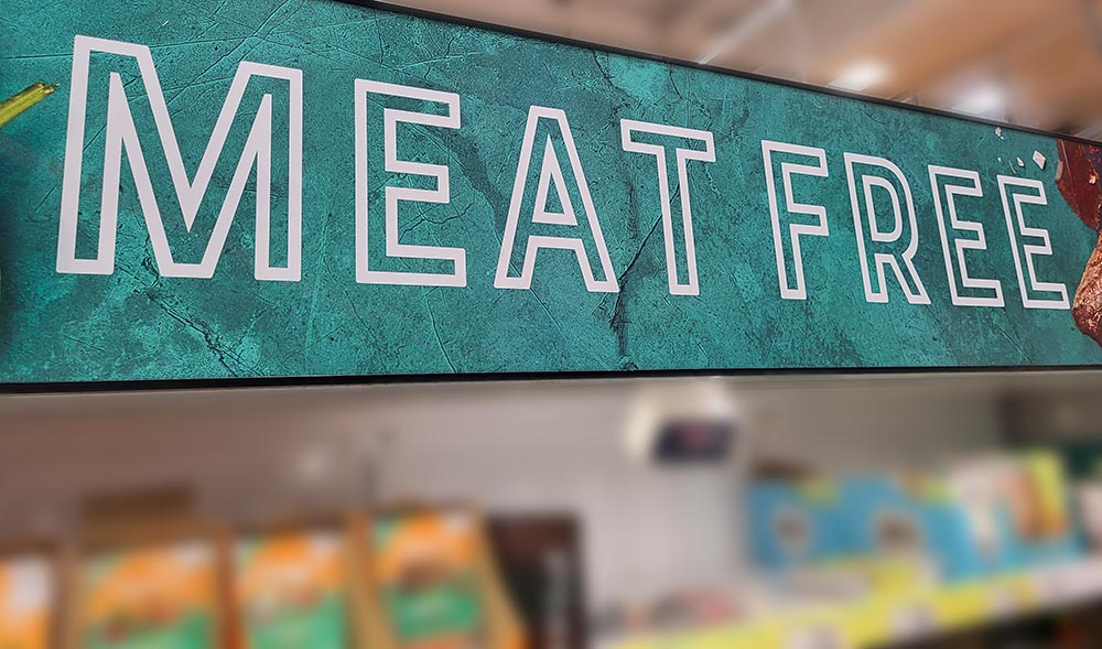 A large sign reading 'Meat-free' hangs above the plant-based meat section of the supermarket. 